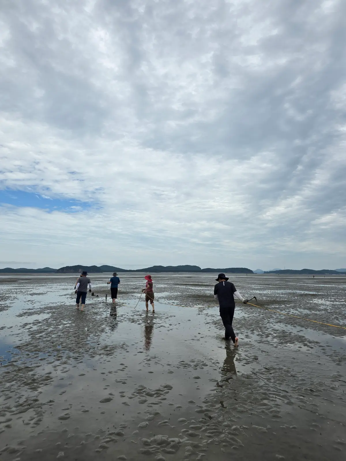 Four people walking across shallow water on a tidal flat beneath dramatic clouds